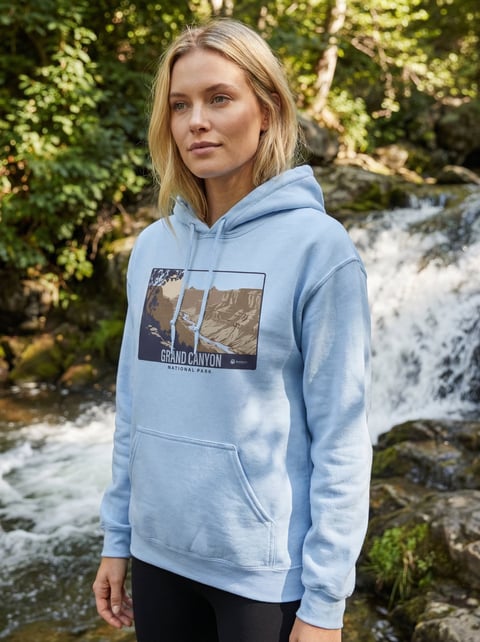 Woman wearing light blue Grand Canyon National Park hoodie standing by a waterfall surrounded by green foliage