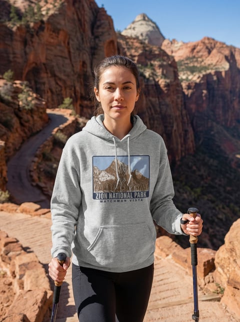 Woman hiking at Zion National Park wearing a gray hoodie and holding trekking poles, surrounded by red rock formations
